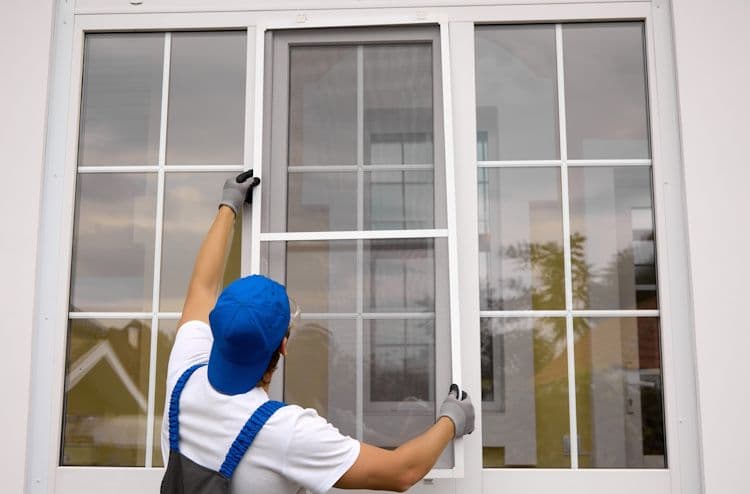 Worker in blue cap and gloves cleaning a large multi-pane window with a squeegee tool